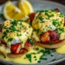 Two poached eggs on English muffins topped with chunks of lobster meat and drizzled with spicy orange-red Cajun hollandaise sauce, garnished with fresh herbs.