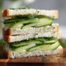 Elegant triangle-cut cucumber sandwiches on white bread with fresh dill garnish arranged on a vintage serving plate.